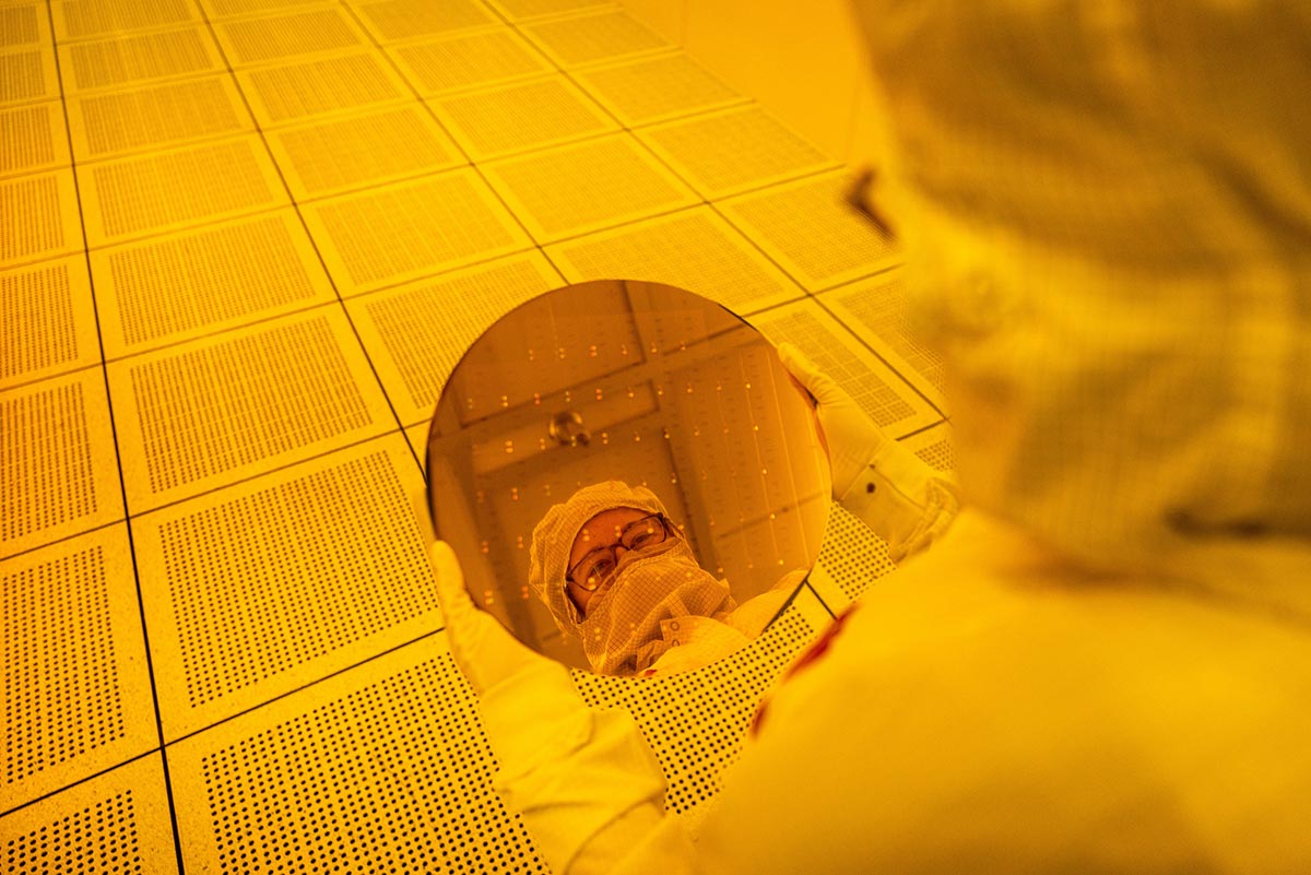 Worker in a fab holding a wafer, and the worker's reflection shows in the wafer.
